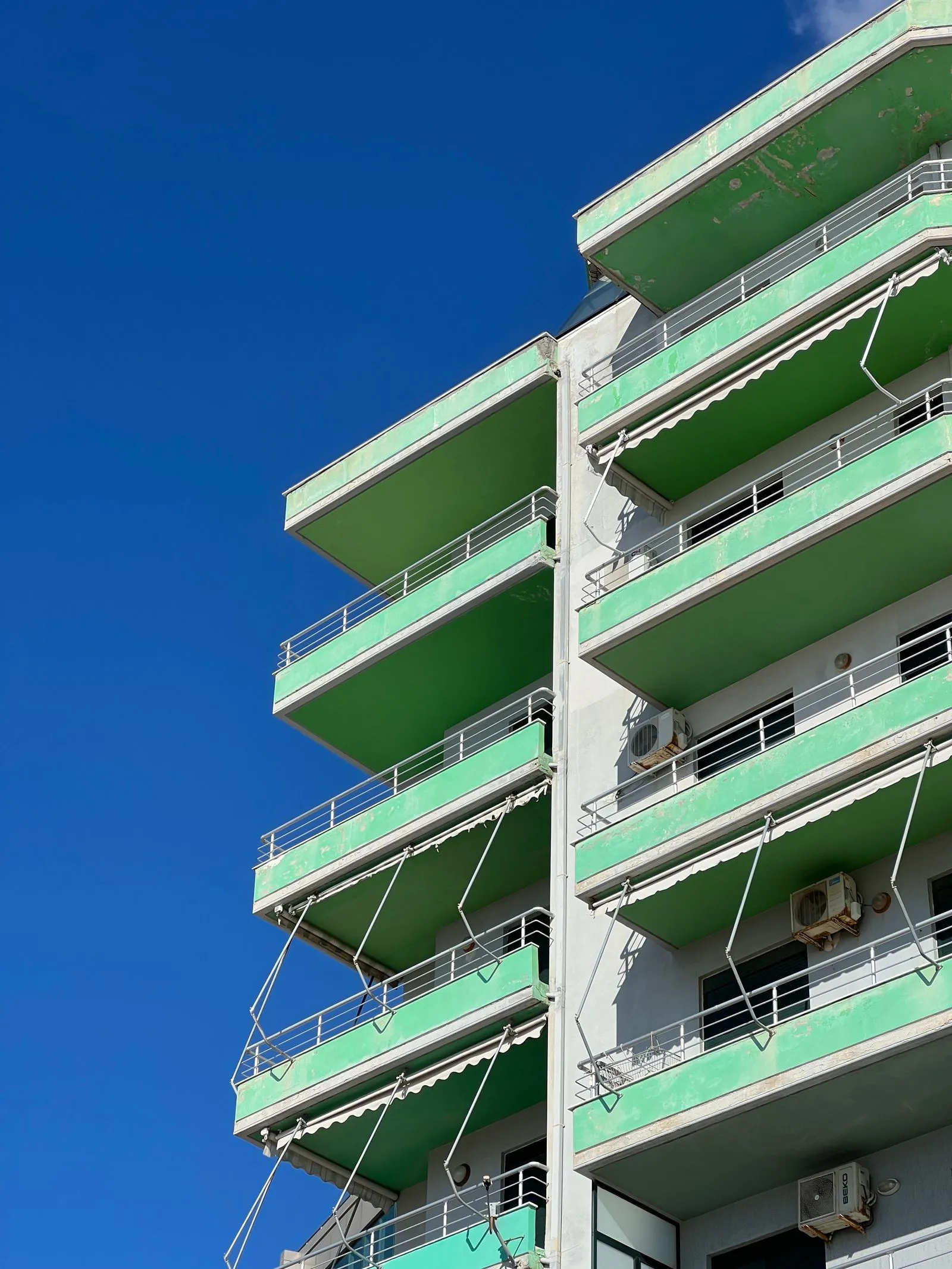 Une résidence aux balcons verts, vue d'en bas sous un ciel bleu