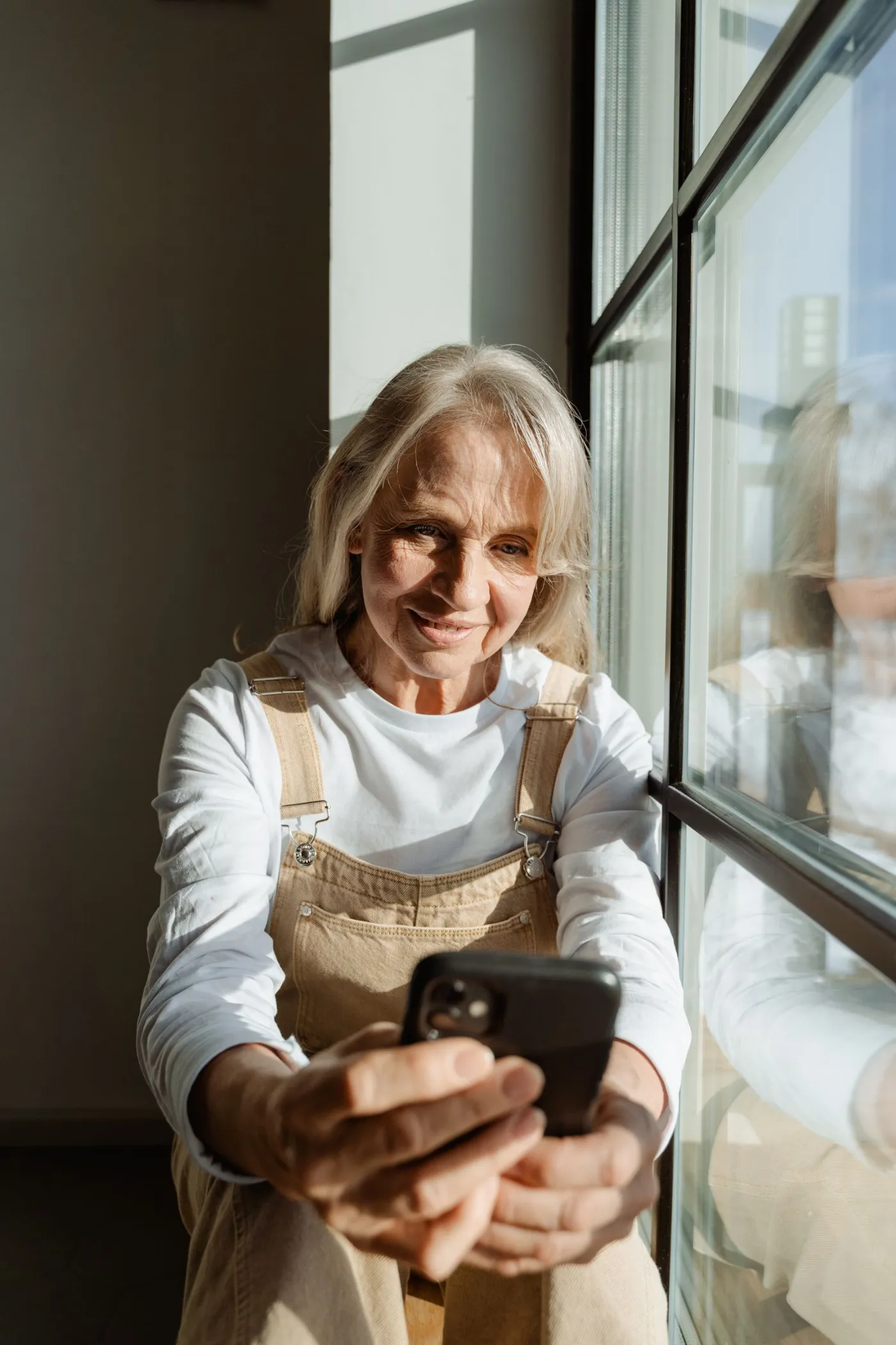 Une locataire souriante regarde son téléphone près de sa fenêtre